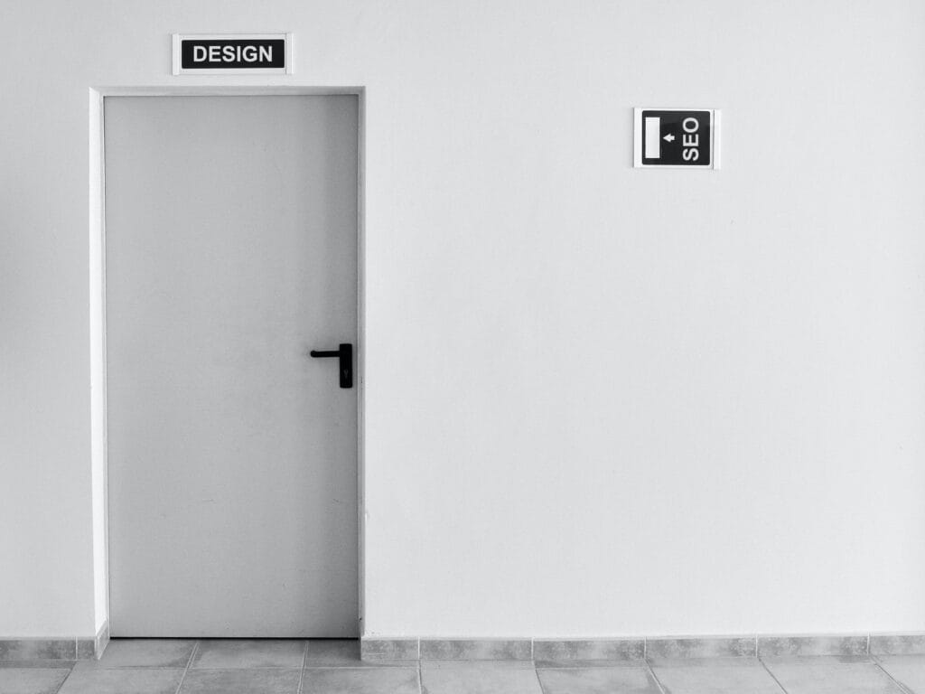 A white office door labeled DESIGN, with a directional sign on the adjacent wall pointing to the SEO department.