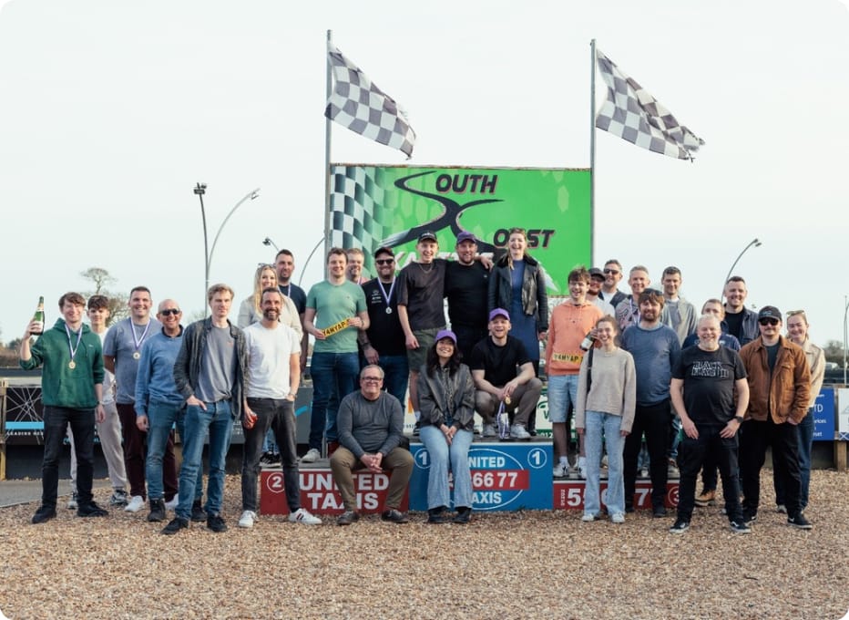 Group of people posing for a photo at South Coast Karting under checkered flags.